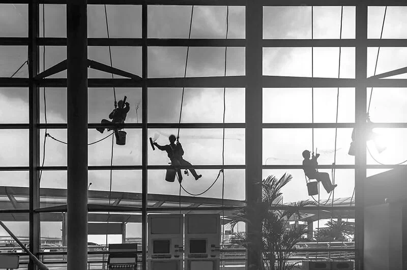 Four window washers suspended on side of very large commercial building washing windows for property maintenance