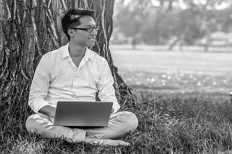 Happy Renters like this Man sitting cross-legged on the lawn, with his back against a tree while holding a laptop