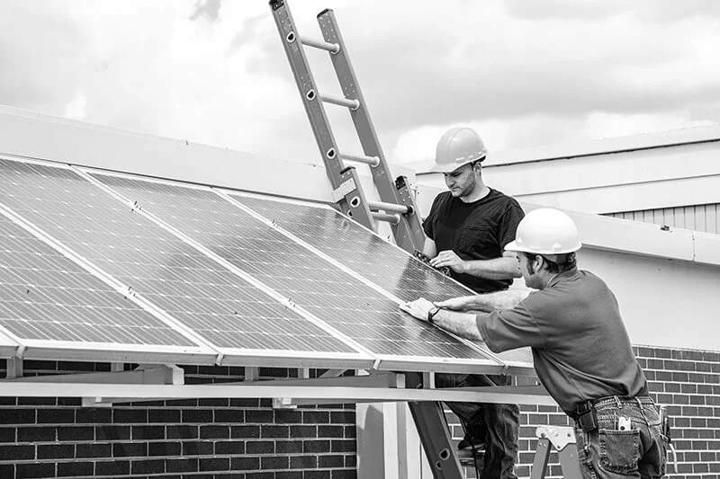 Two men working together installing solar panels on side of building from energy saving tips