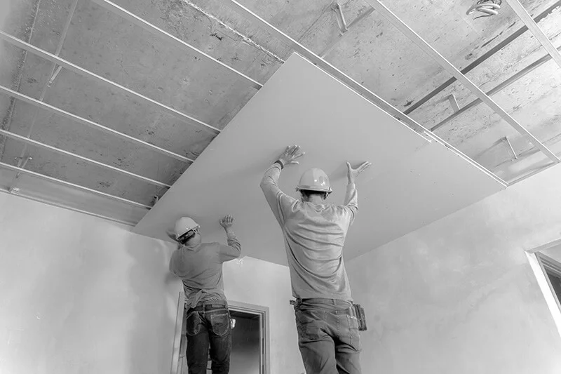 Two men hanging new drywall on ceiling for better tenant improvement