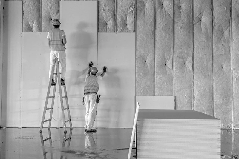Two men working together to install drywall panels for construction services